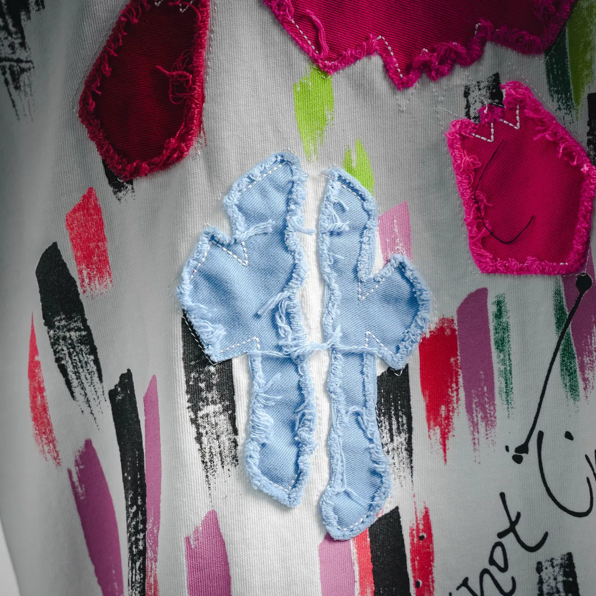 White T-shirt with layered embroidered heart-like patches in pink, blue, and red