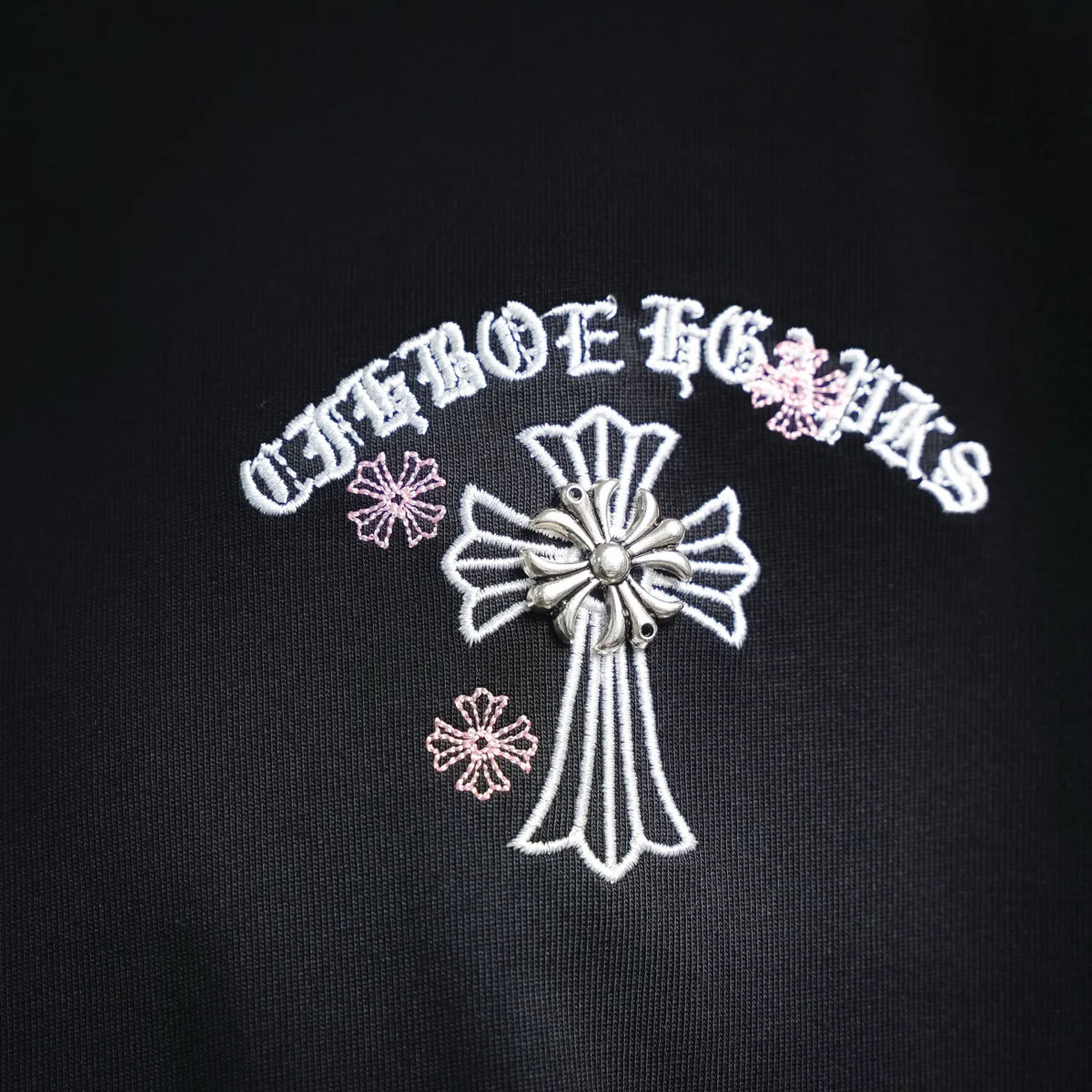 Close-up of white and pink embroidered cross on black T-shirt chest.