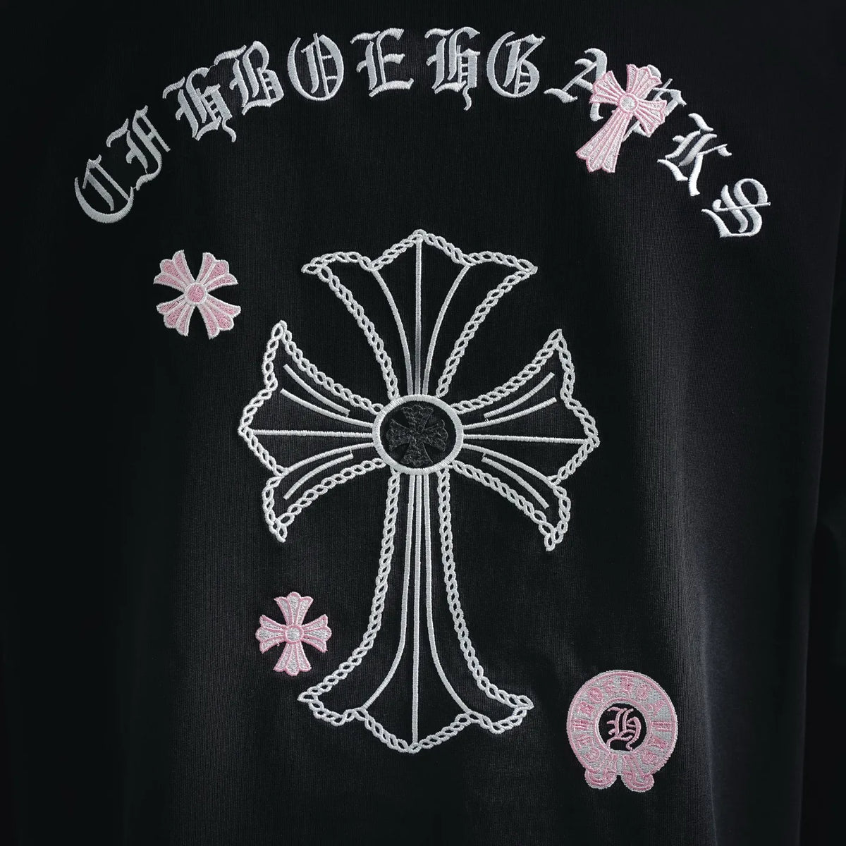 Back embroidery close-up: white cross design with pink accents and round patch.