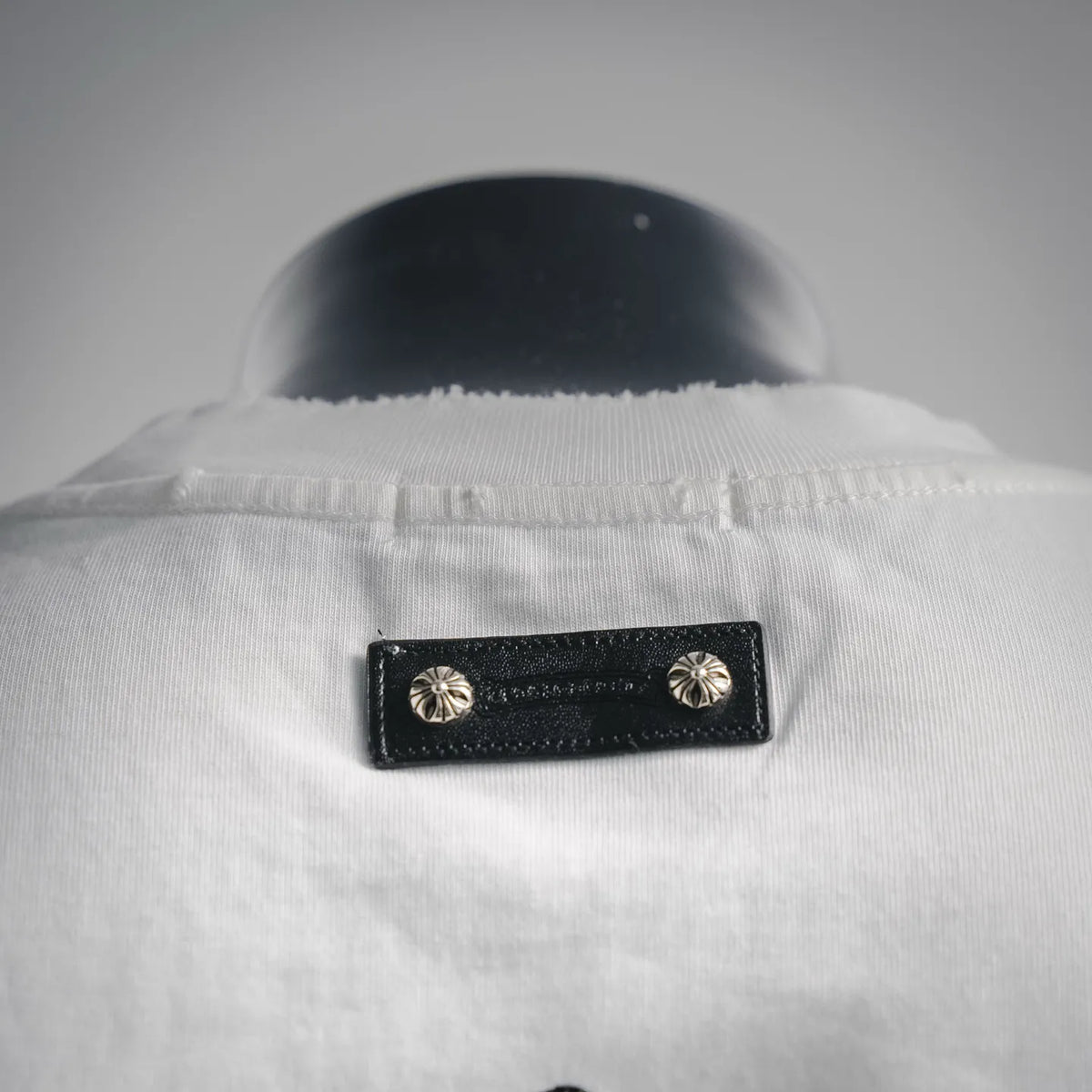 White T-shirt neckline with black fabric tag and metallic button details