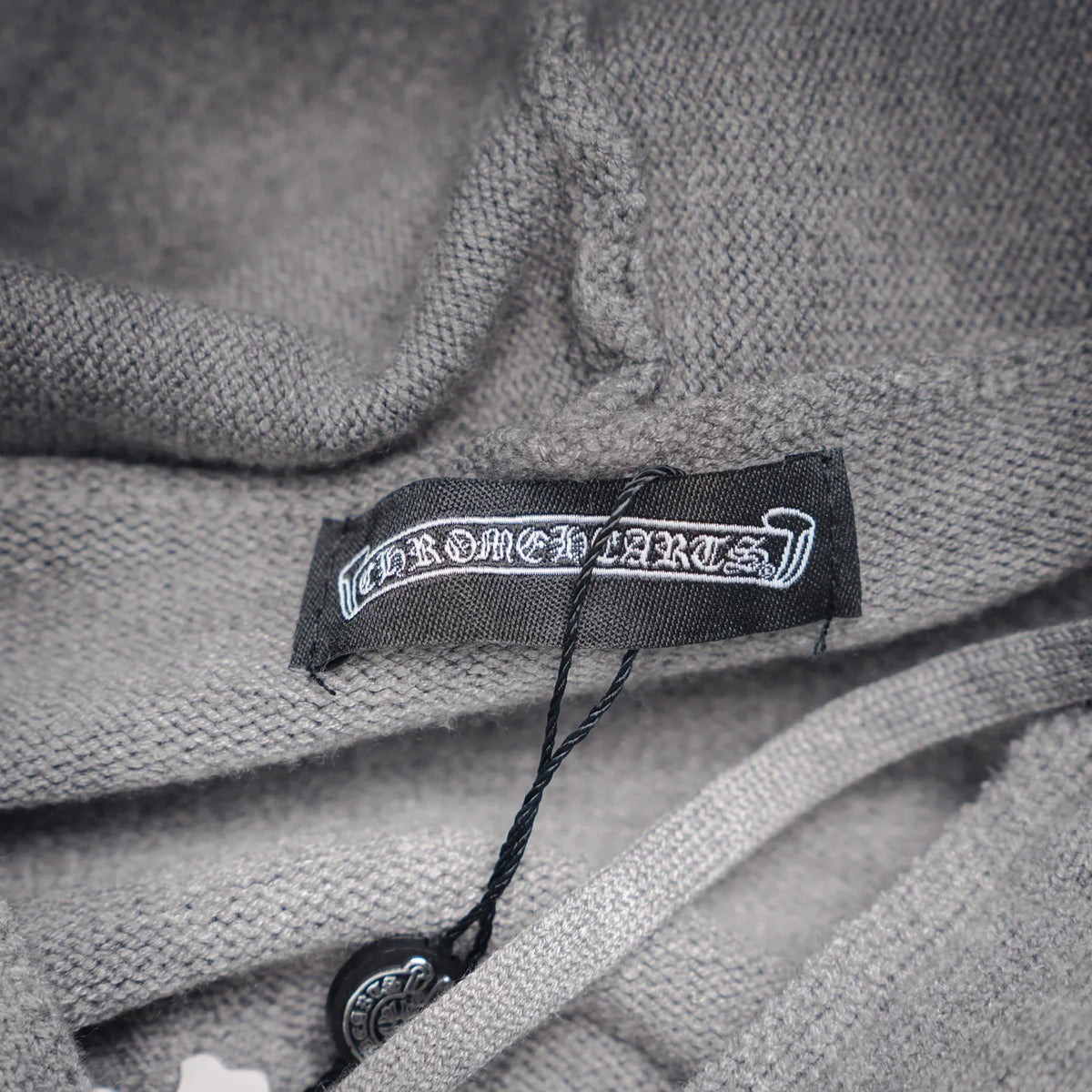 Light gray hoodie neck label with black brand tag and drawcord.