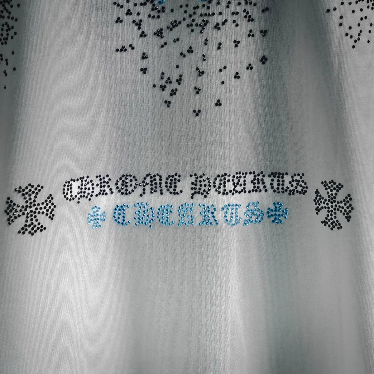 Close-up of rhinestone text and snowflake dots on a white T-shirt