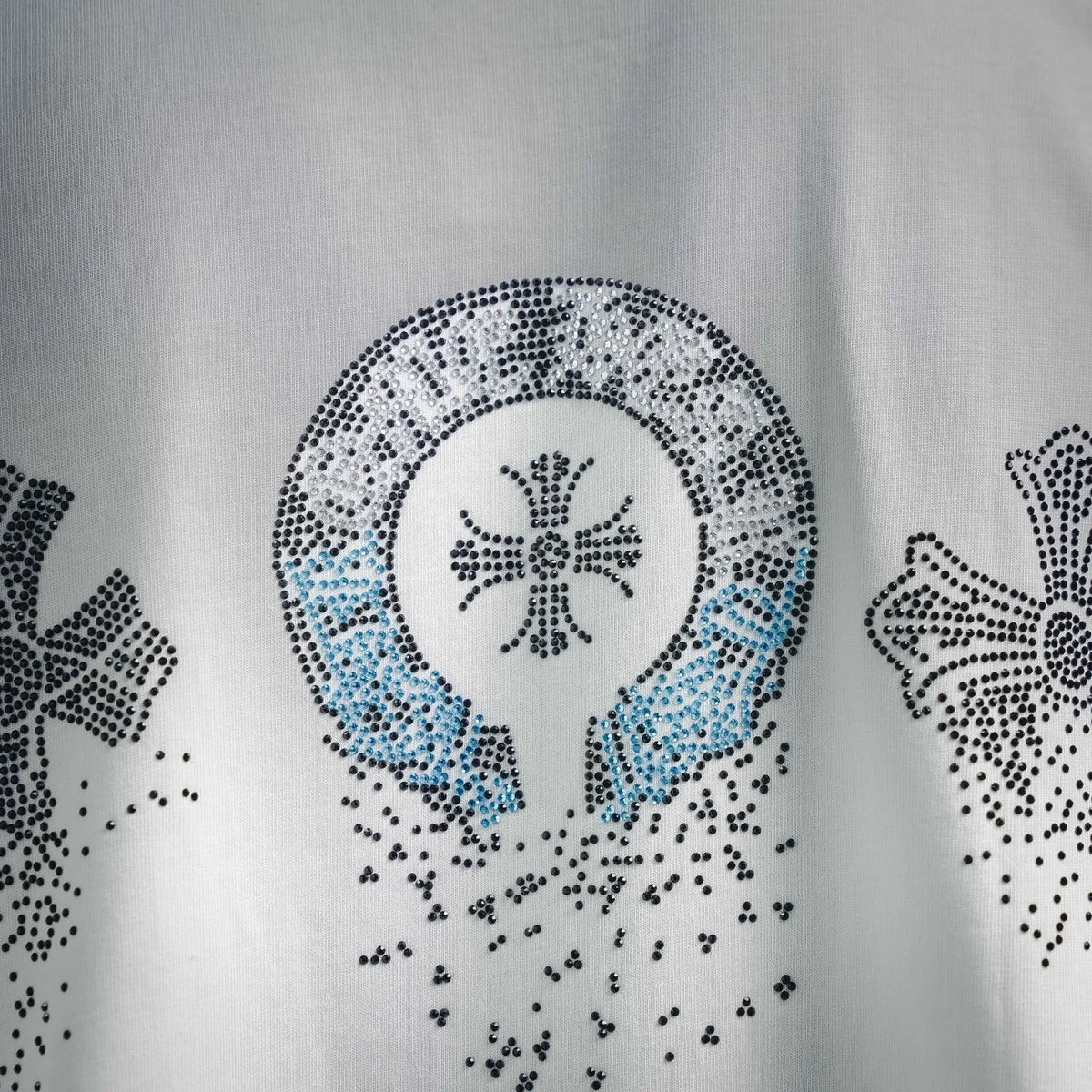 Close-up of rhinestone emblem with blue accents on a white T-shirt