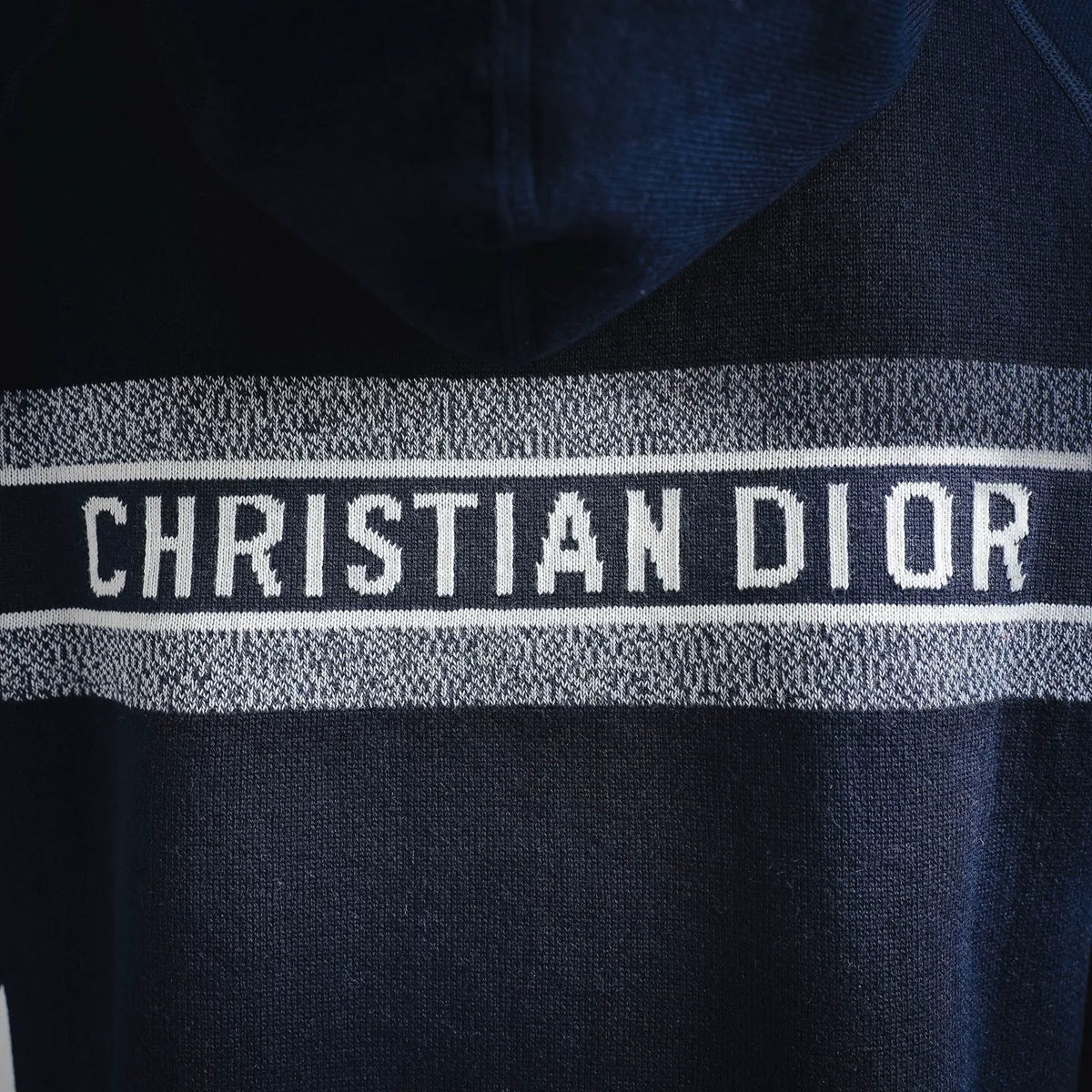 Close-up of "CHRISTIAN DIOR" logo stripe on navy knit hooded coat