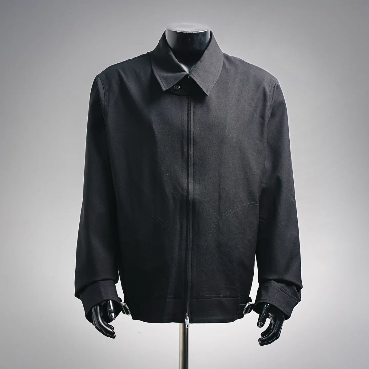 Black zip-up coat with pointed collar, front placket, and long sleeves