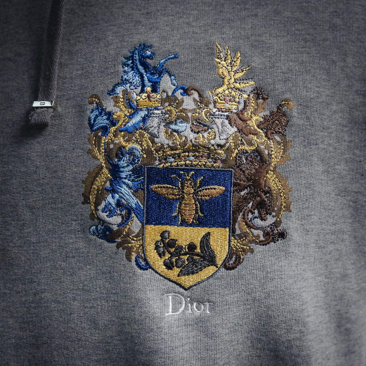 Gray hoodie with large embroidered crest emblem on chest and small "Dior" text below