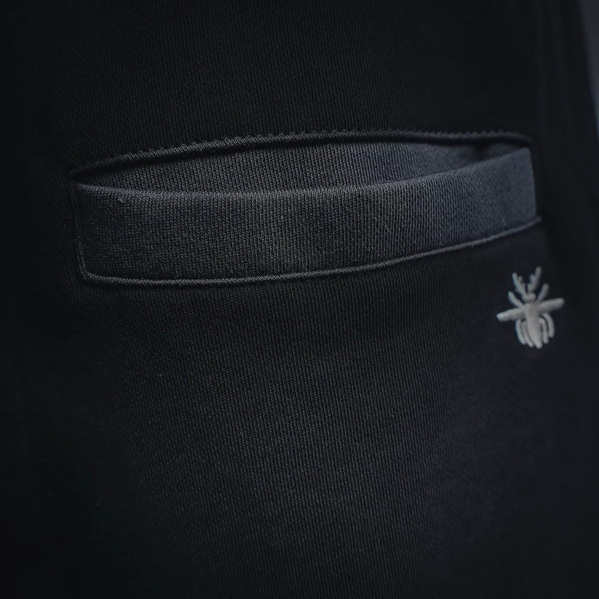 Black shorts front pocket with small embroidered emblem, close-up