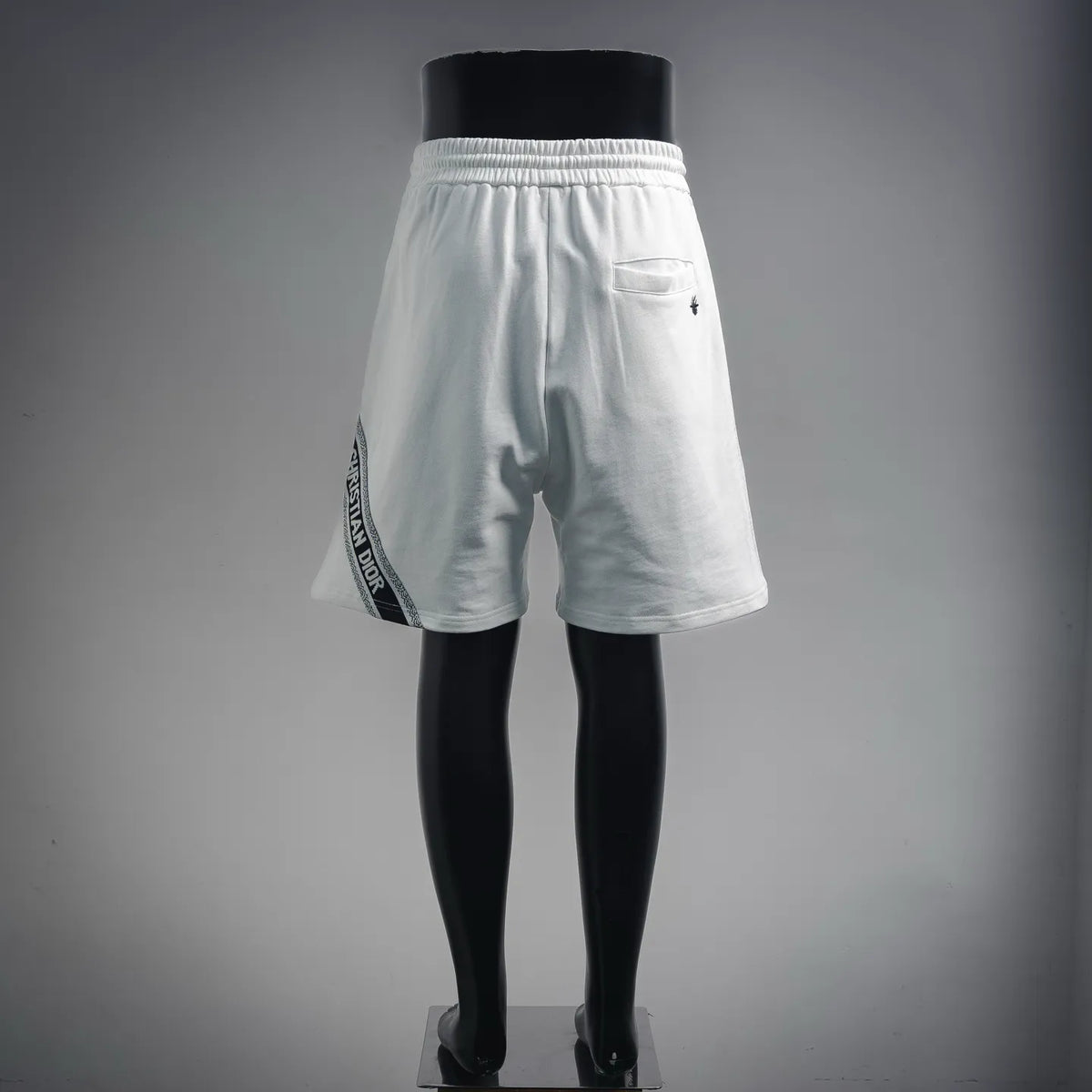 White shorts back view with elastic waistband, pocket, and embroidered logo badge