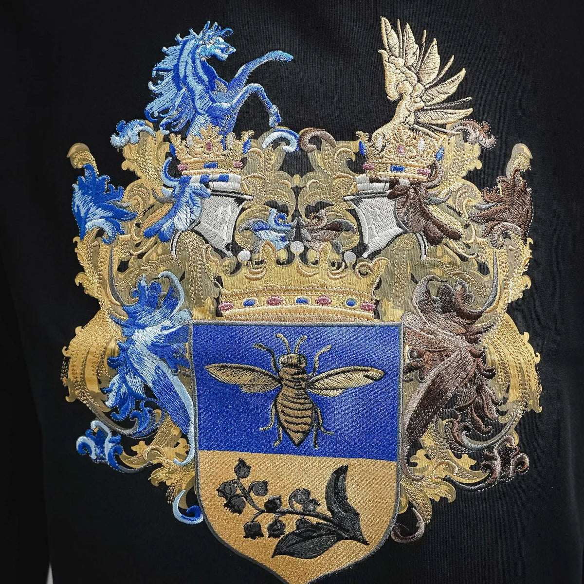 Black T-shirt featuring ornate blue, gold, and beige crest embroidery