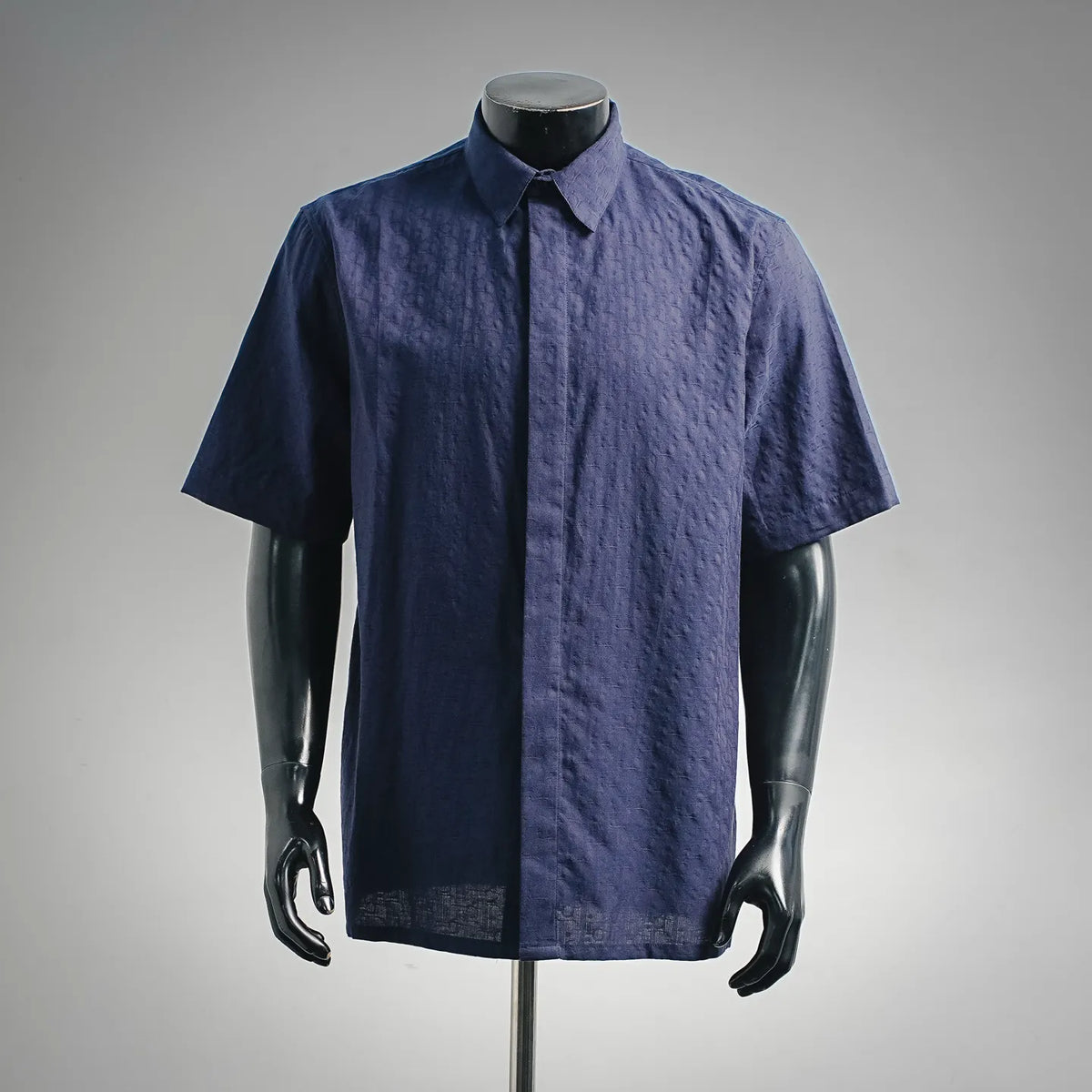 Navy short-sleeve button-up shirt on a mannequin, pointed collar, center front placket.