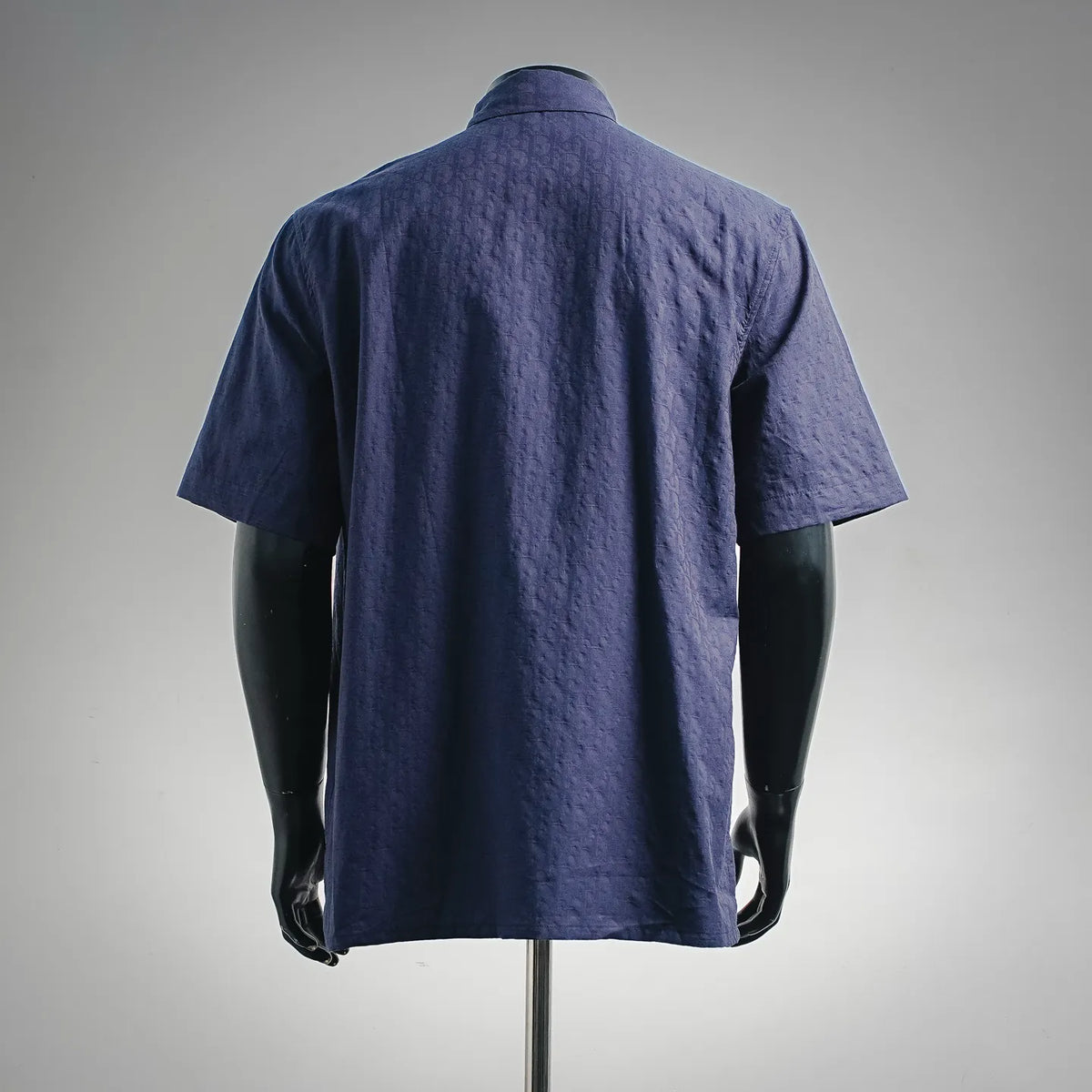 Navy short-sleeve button-up shirt back view, smooth shoulders and yoke, curved hem.