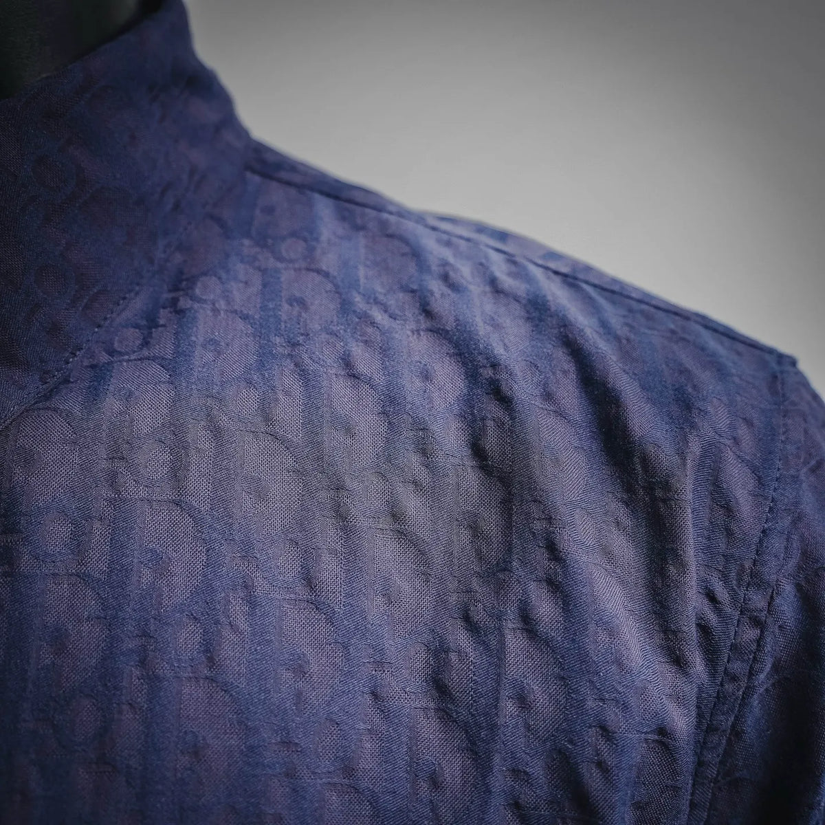 Navy short-sleeve shirt with textured fabric and faint Dior monogram pattern.