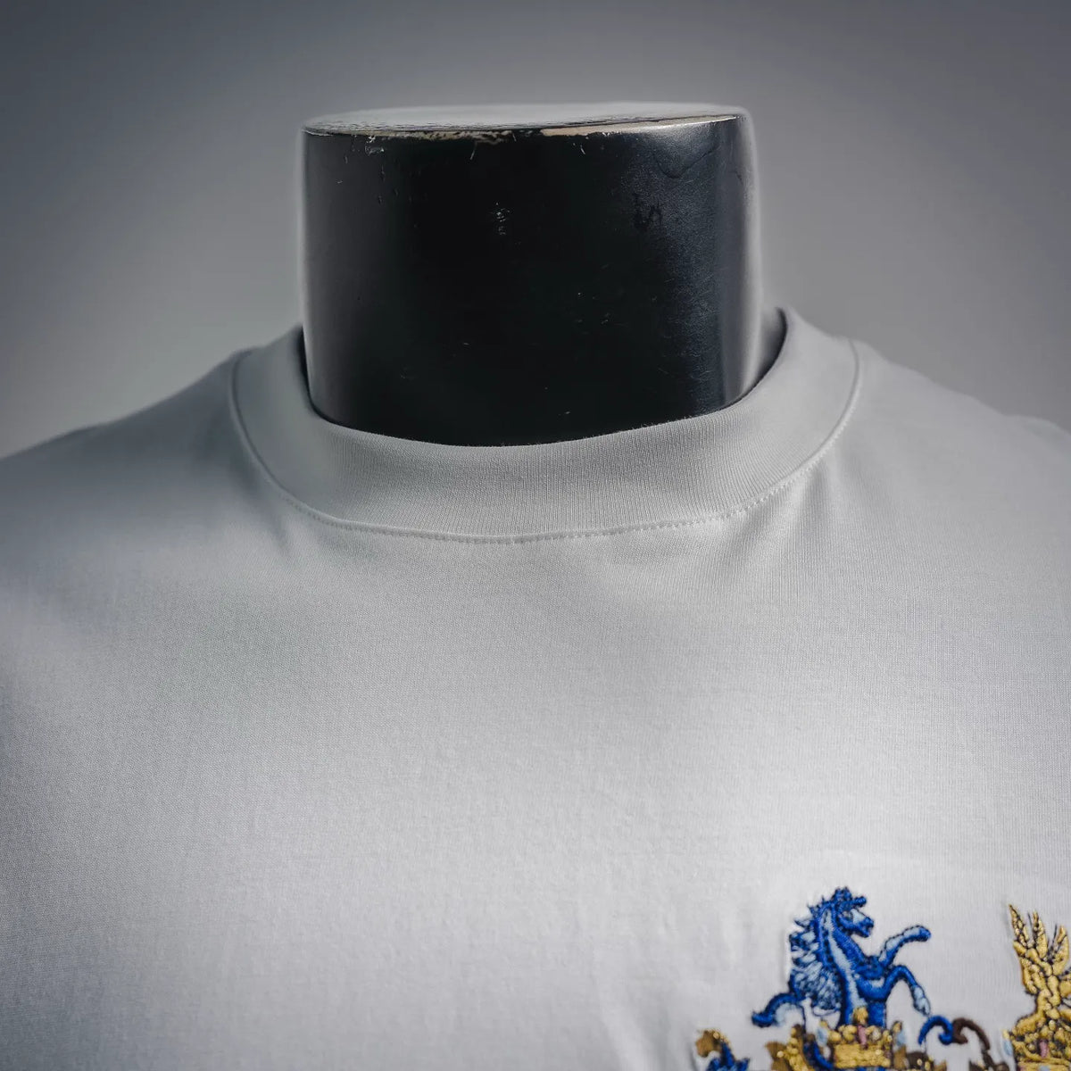 White T-shirt close-up of crew neckline with embroidered crest detail