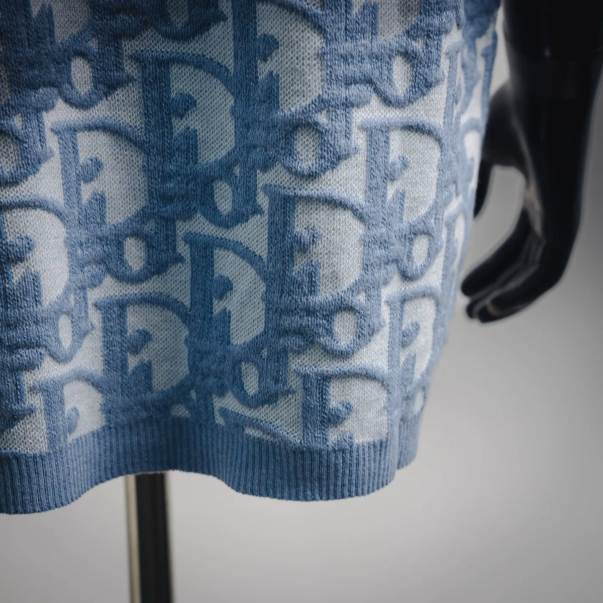 Light blue knit sweater hem with ribbed trim and repeating Dior pattern.