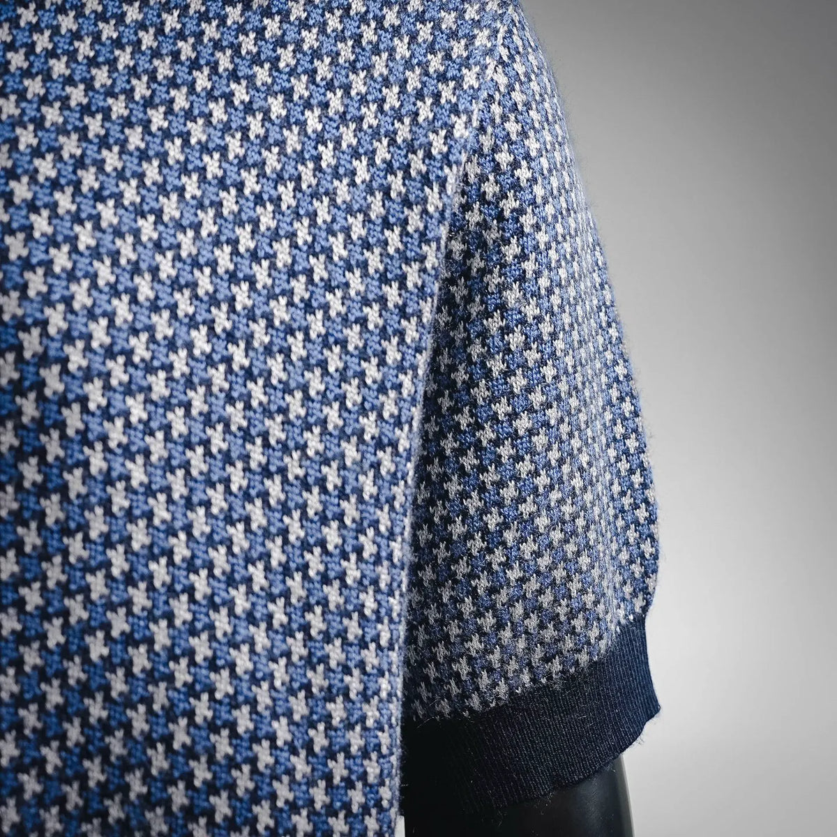 Side view of blue and white houndstooth knit sweater with ribbed cuff and hem