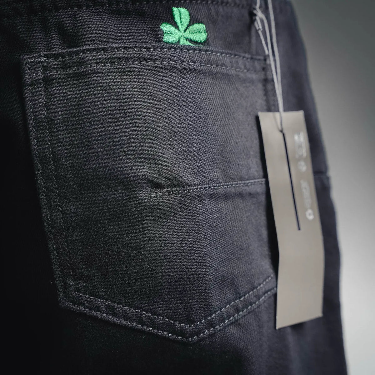 Black pocket detail with green clover embroidery and stitched seams