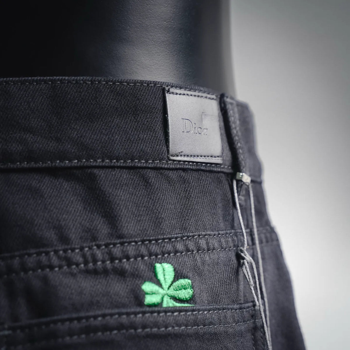 Black pants waistband label and green clover patch near pocket