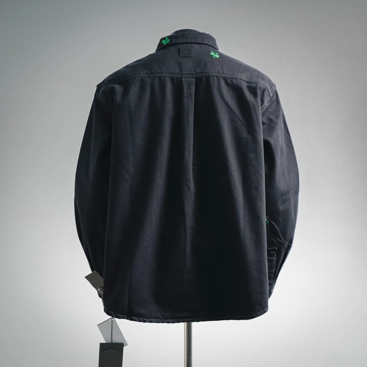 Black long-sleeve button-up shirt on mannequin, back view with small green clover details