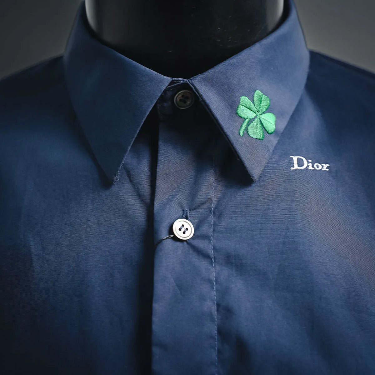 Dior short-sleeve shirt neckline close-up: dark blue collar, green clover patch, button