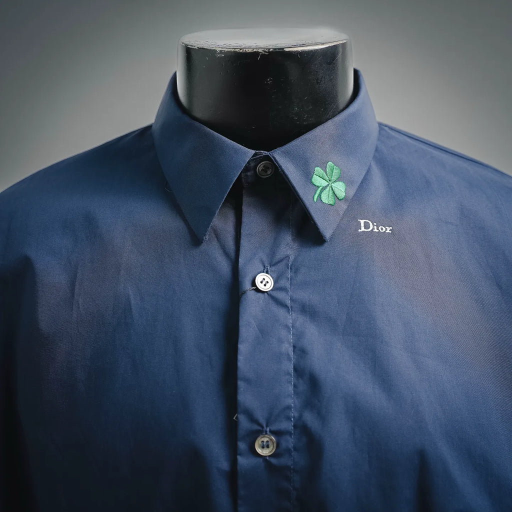 Dior dark blue short-sleeve button-up shirt on mannequin with green clover pin and collar logo