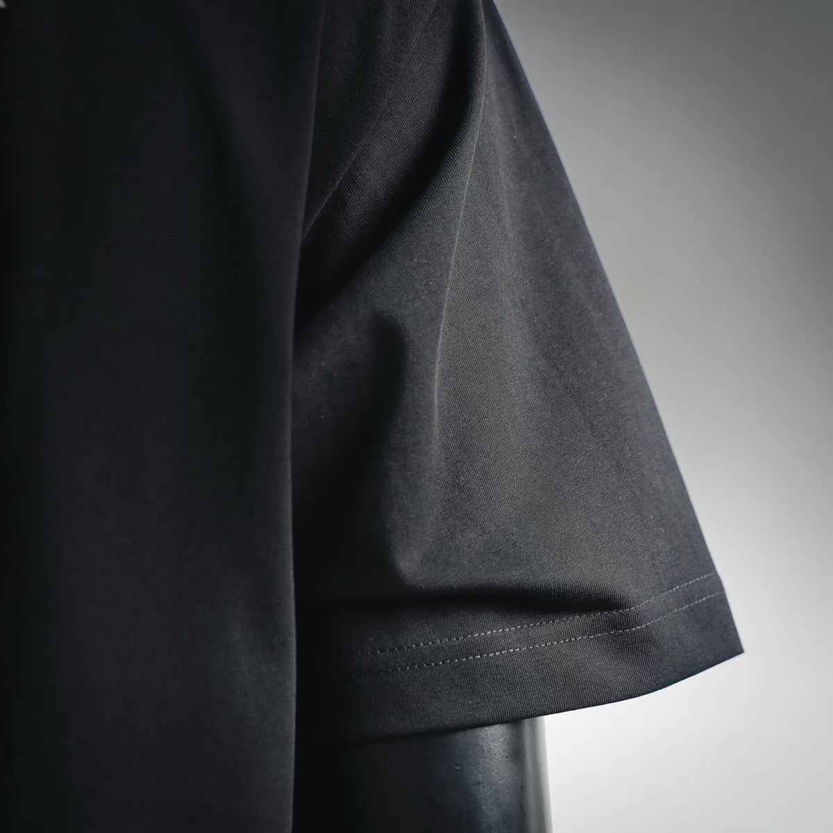 Dior T-shirt sleeve hem detail with stitched cuff and dark fabric texture.