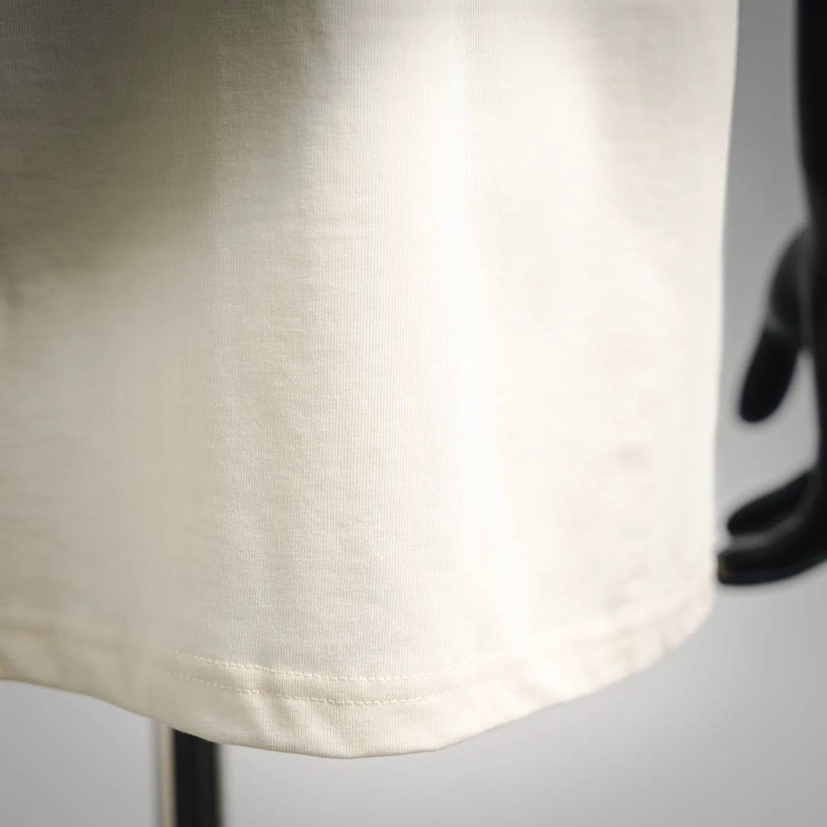 Cream T-shirt fabric close-up with stitched hem and smooth knit texture