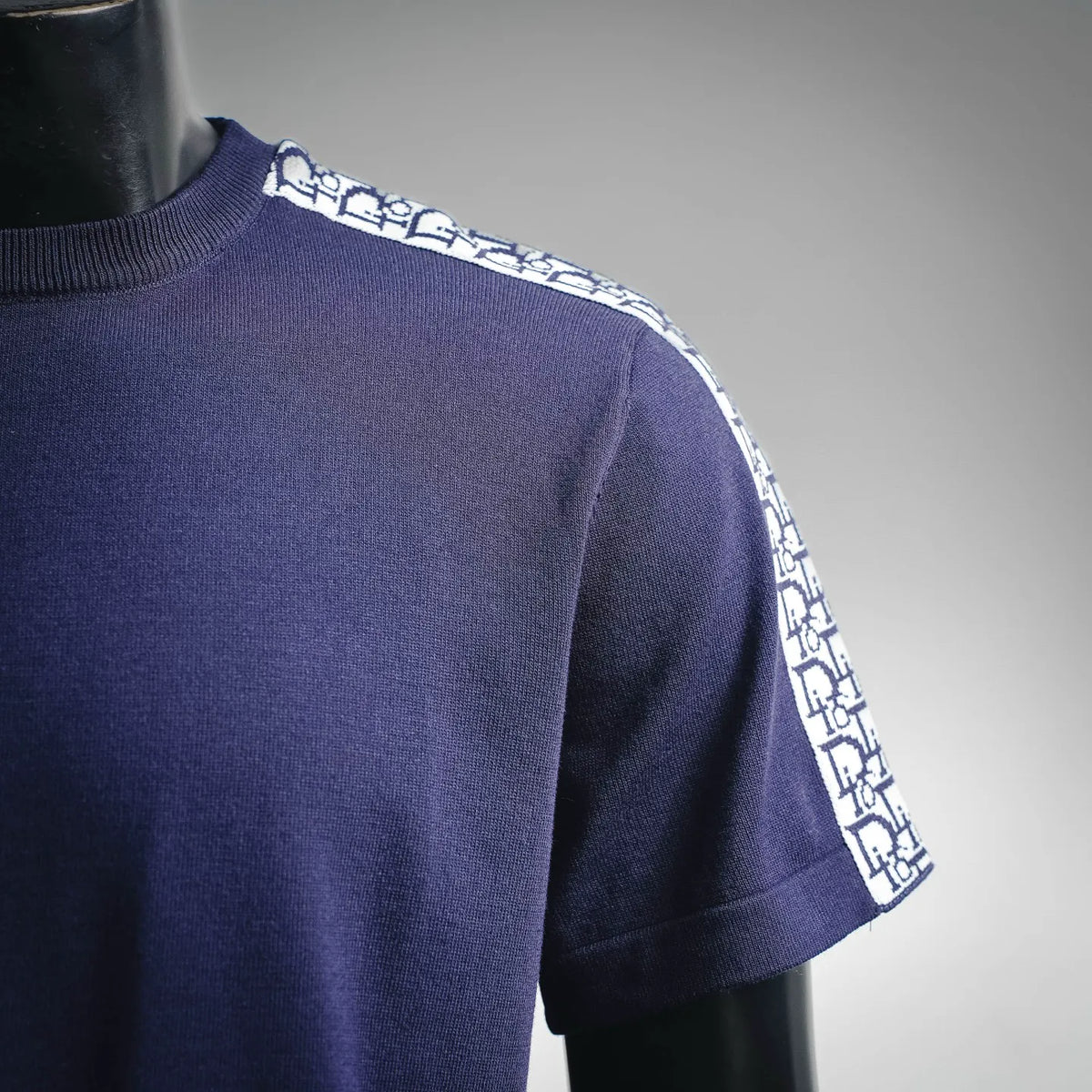 Navy T-shirt shoulder with white Dior logo stripe along sleeve seam.