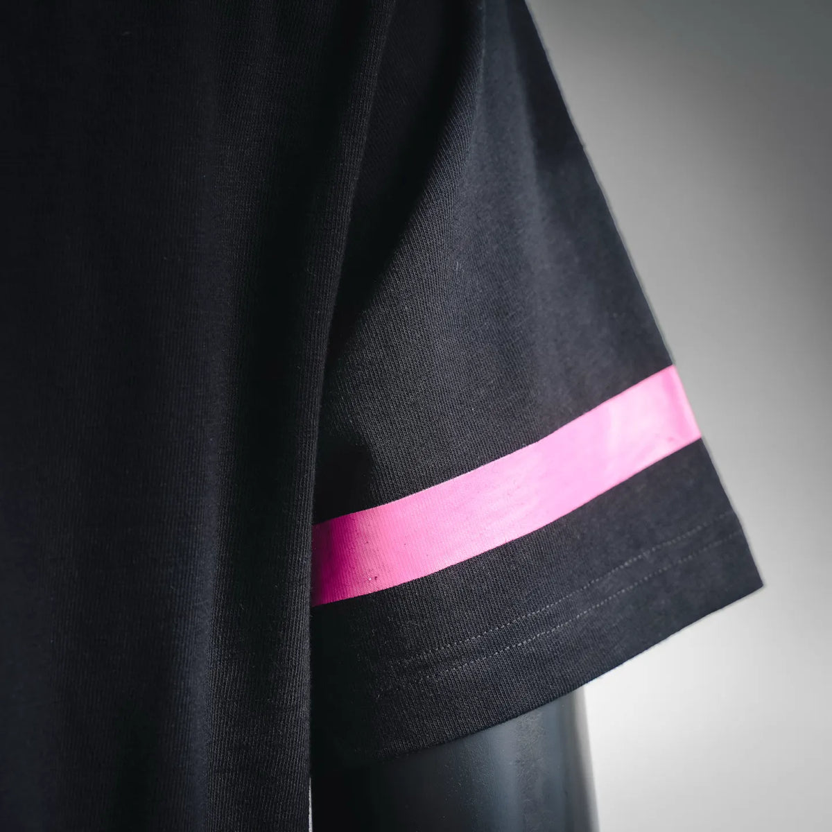 Close-up of black T-shirt sleeve with pink stripe band at hem