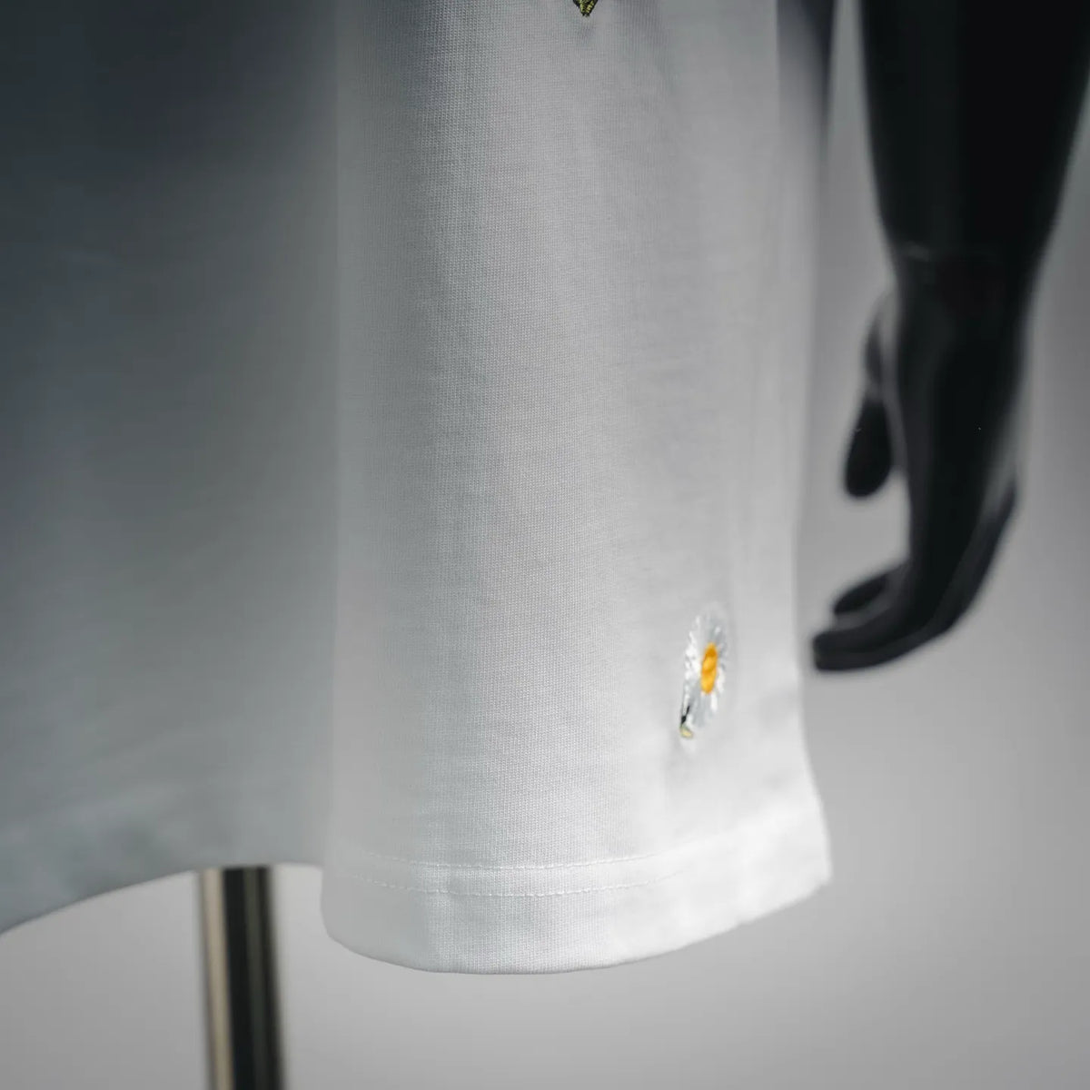White T-shirt fabric close-up with small daisy embroidery near hem