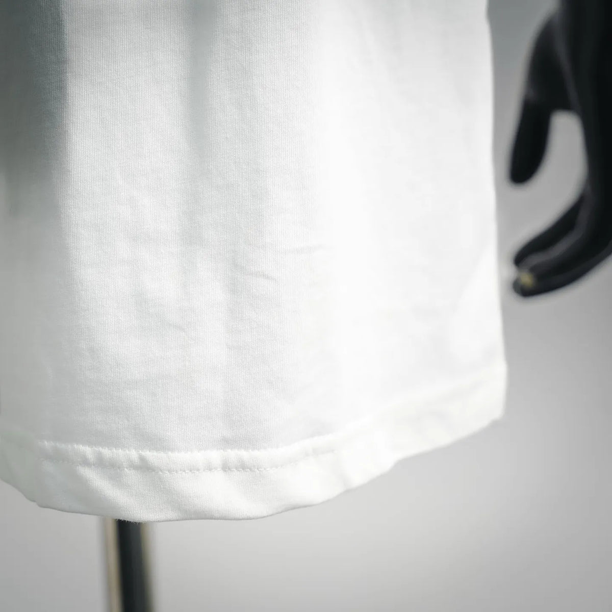 White crew-neck T-shirt fabric close-up with stitched hem detail