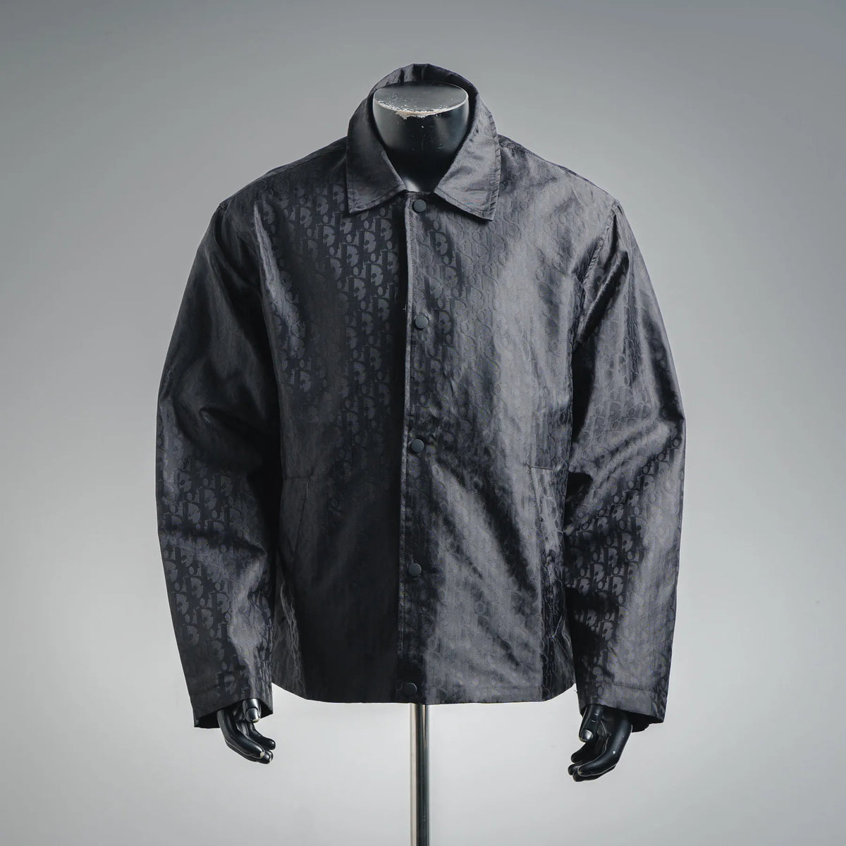 Dark monogram jacket coat with stand collar and zip-front closure on a mannequin