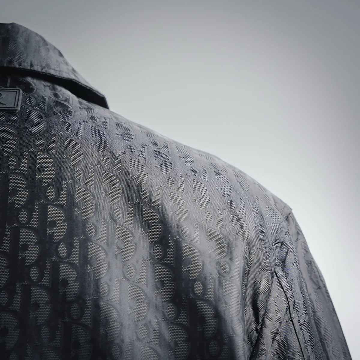 Close-up of dark monogram coat sleeve and shoulder with subtle textured sheen