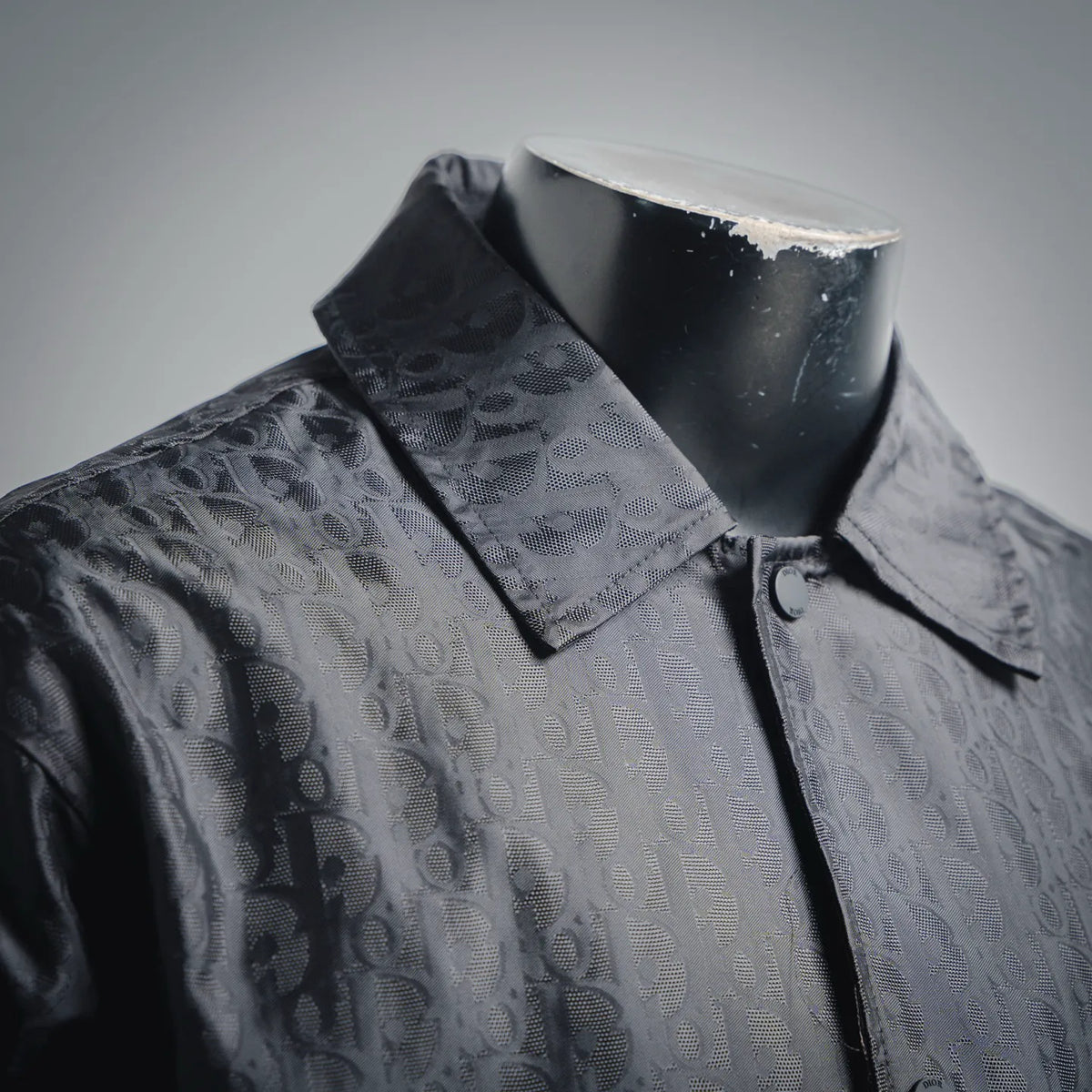 Dark monogram coat with stand collar, front zip, and button accents near placket