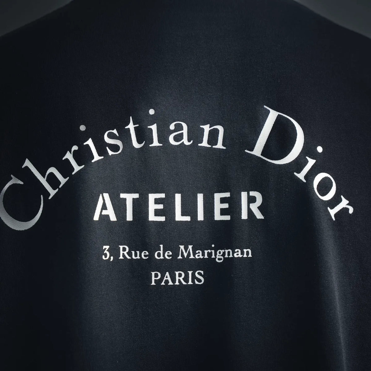 Close-up of white Dior Atelier back logo text on black T-shirt