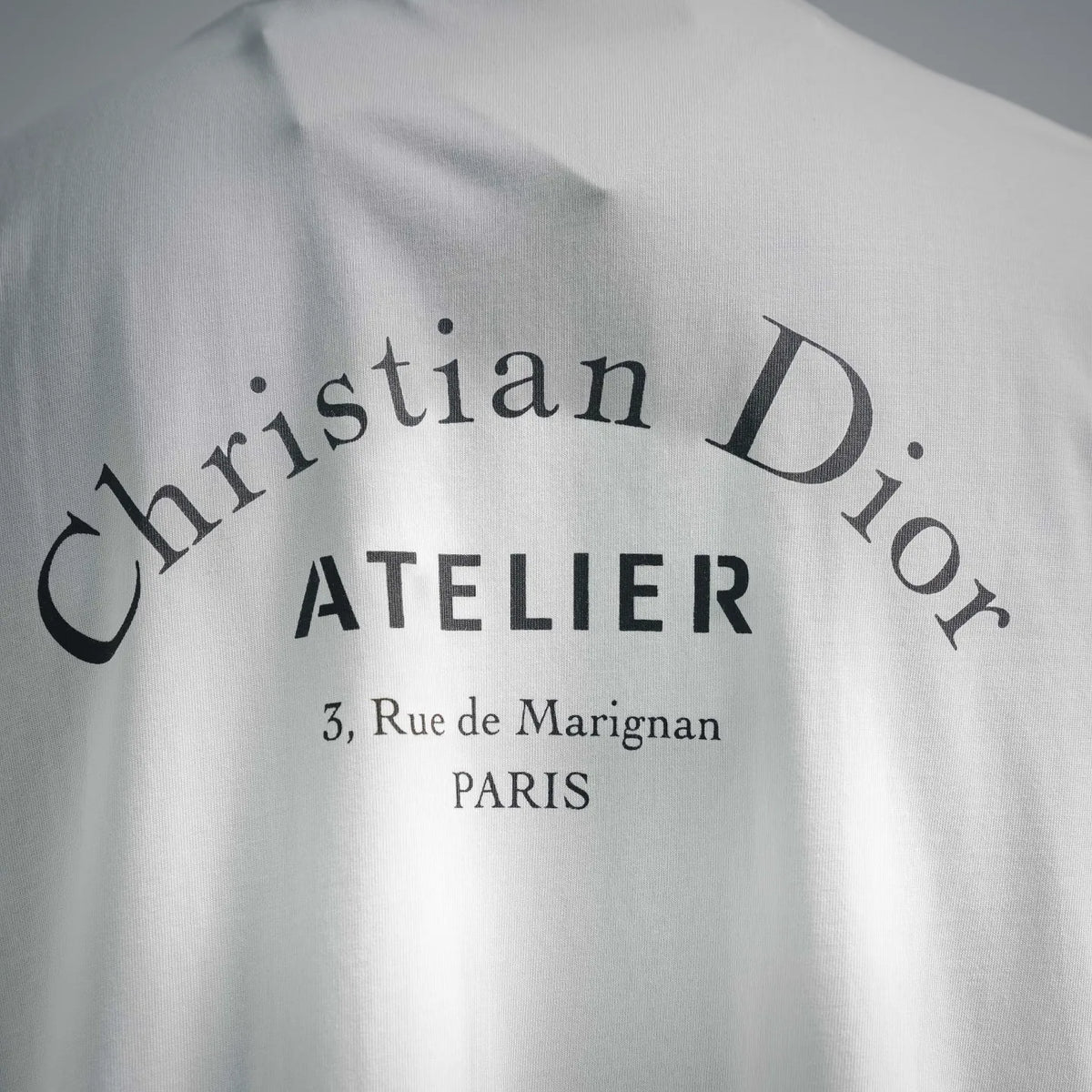 Close-up of Dior Atelier logo text on white short-sleeve T-shirt