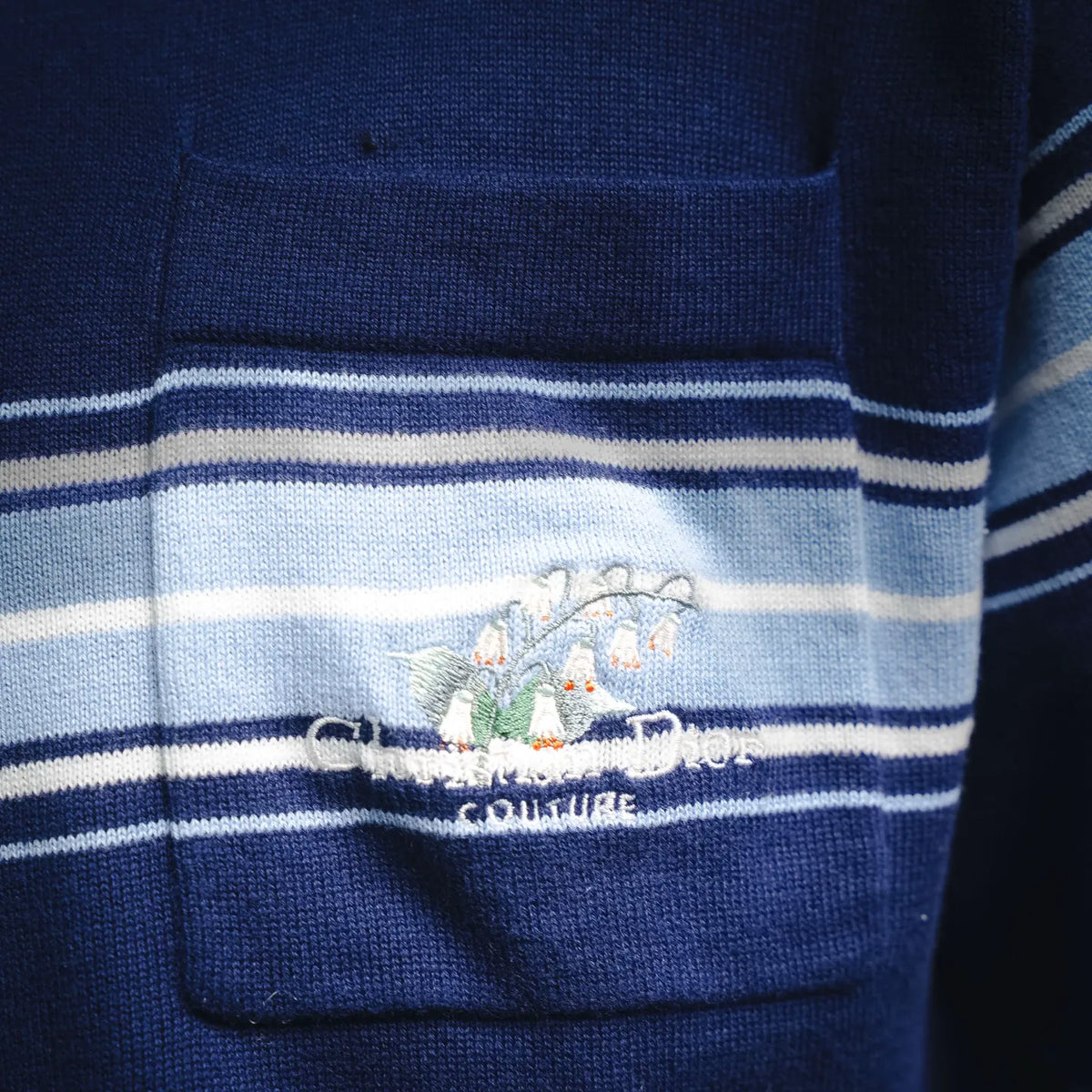 Blue polo chest pocket with embroidered logo and white striped bands