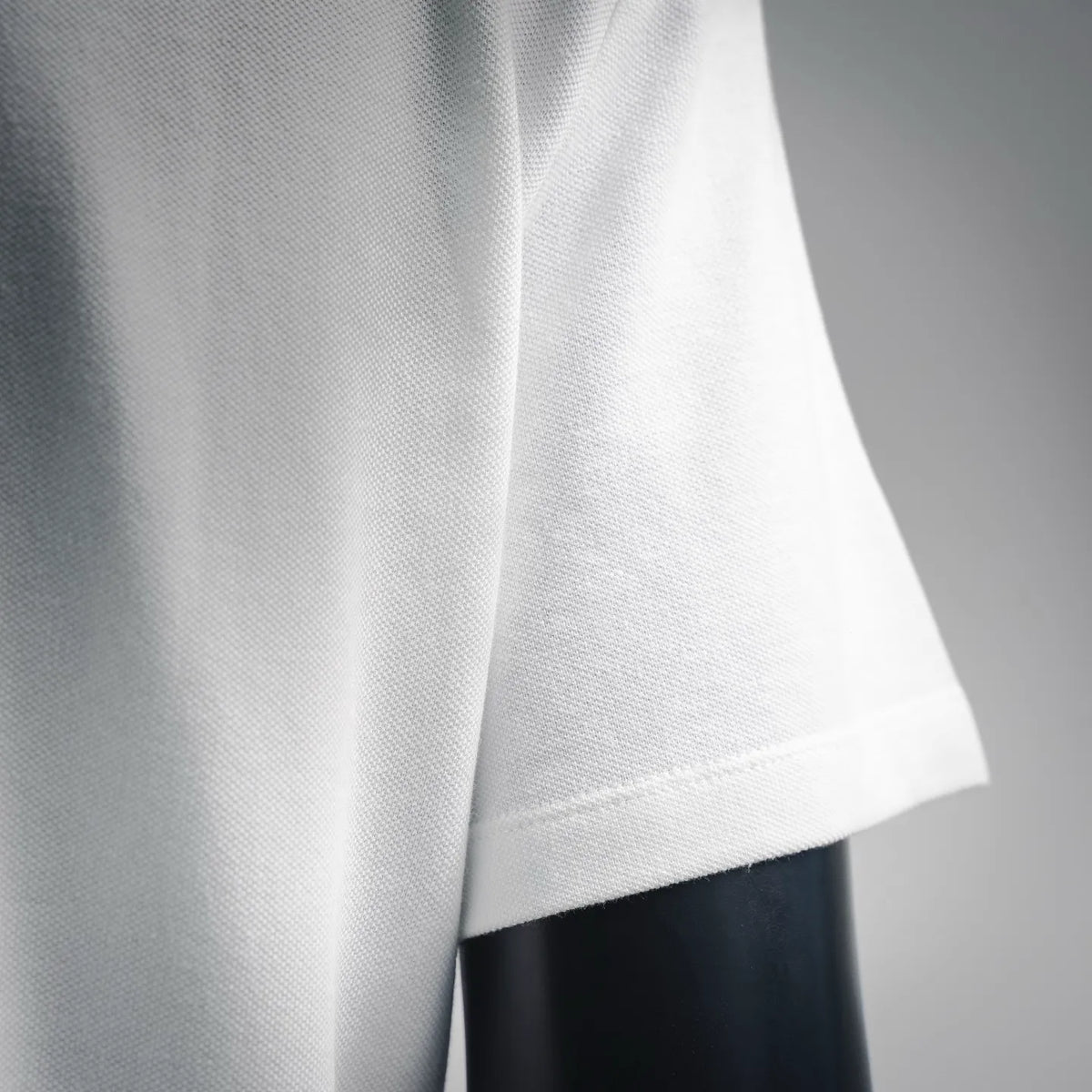 White polo shirt side fabric close-up with stitched curved hem edge.