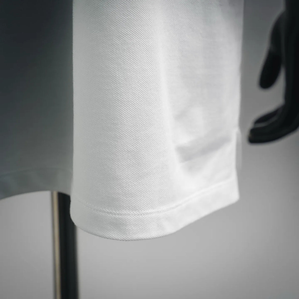 White polo shirt sleeve and lower hem close-up with neat stitched edge.