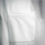 White Dior polo shirt chest pocket area close-up with Dior embroidery.