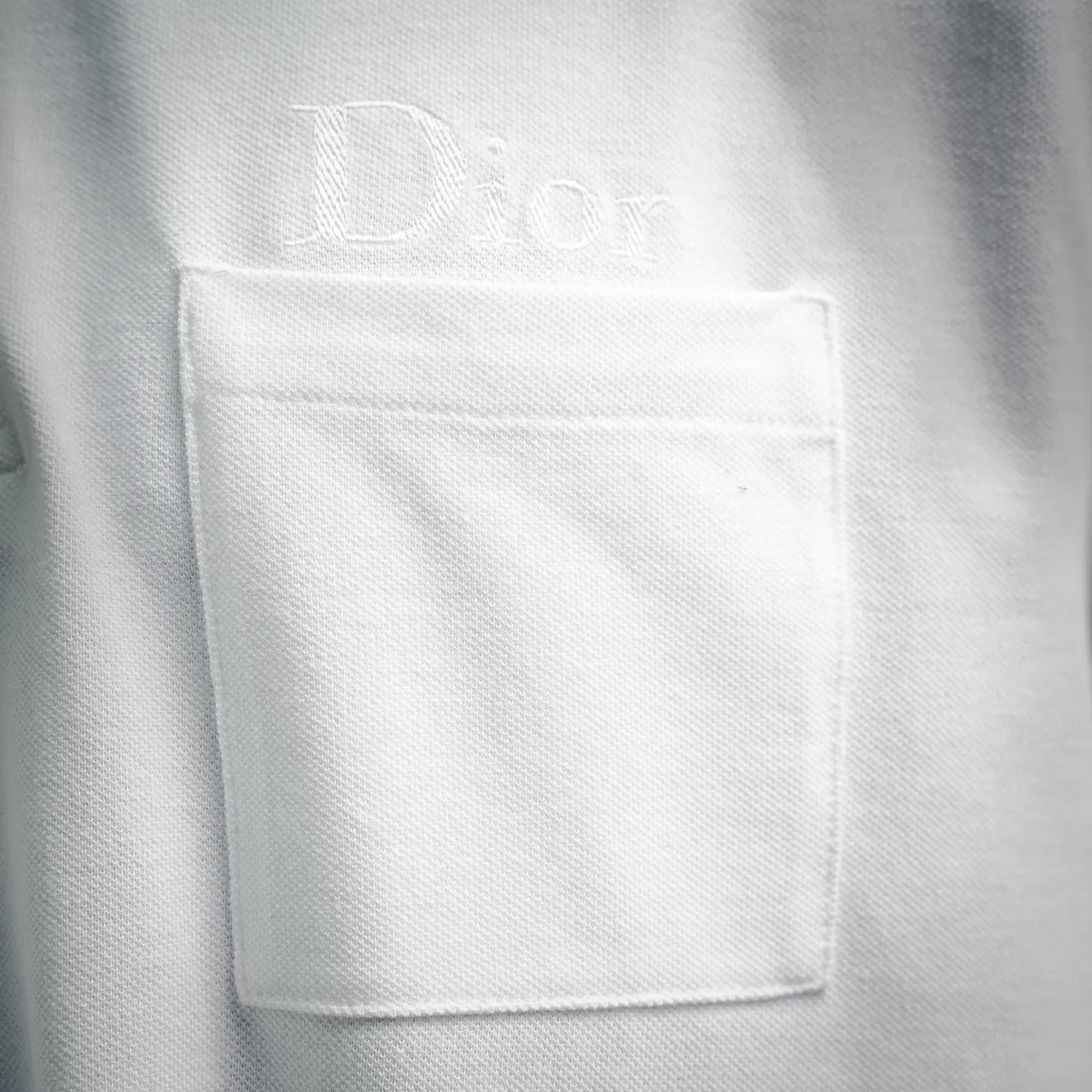 White Dior polo shirt chest pocket area close-up with Dior embroidery.