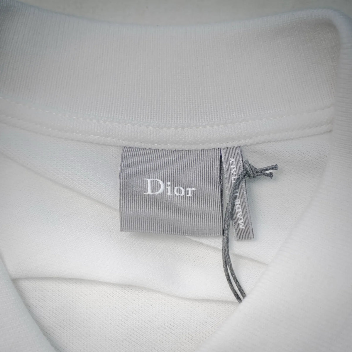 White Dior polo shirt neck label reading “Dior” with ribbon tie.