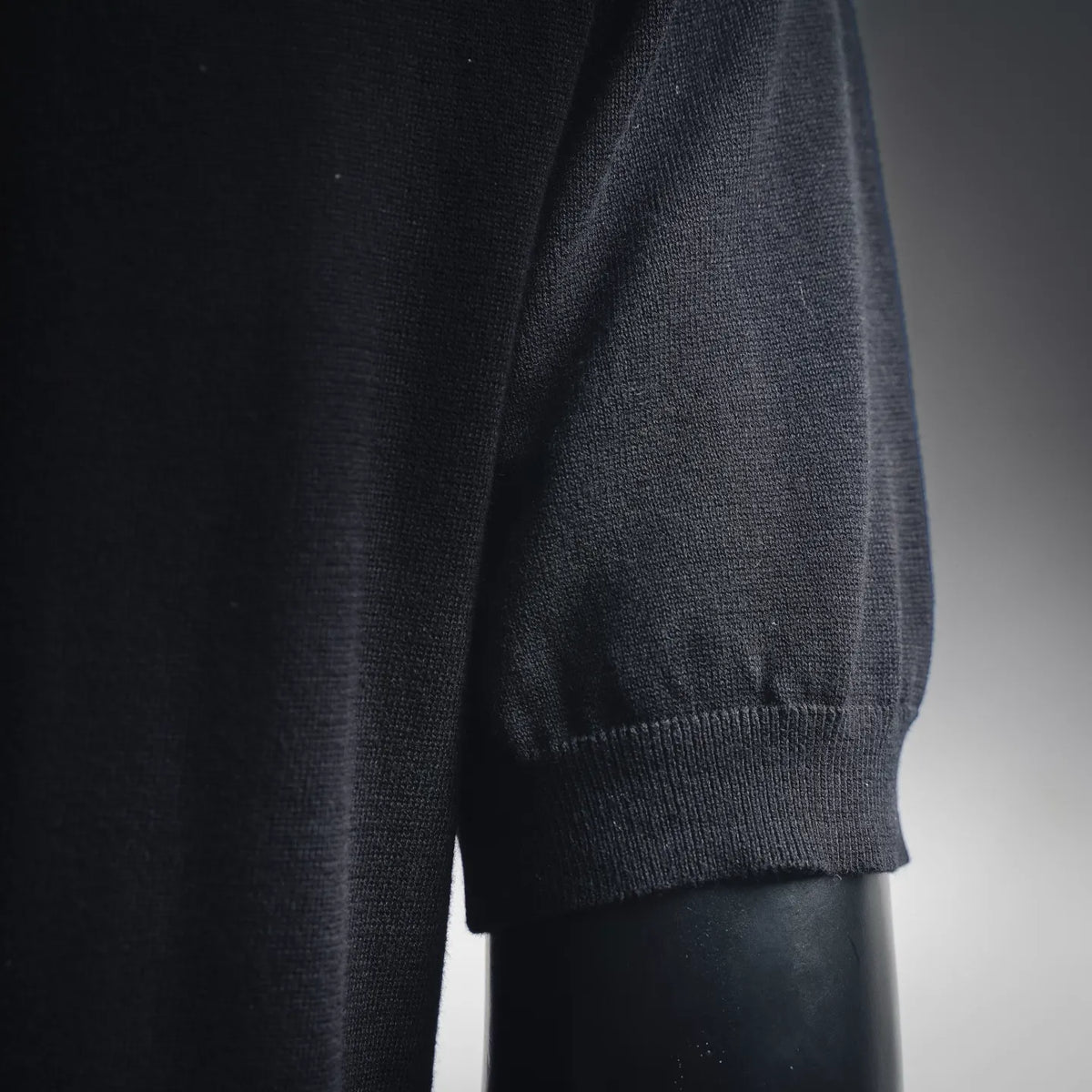 Black polo knit shirt sleeve cuff and side seam; close-up