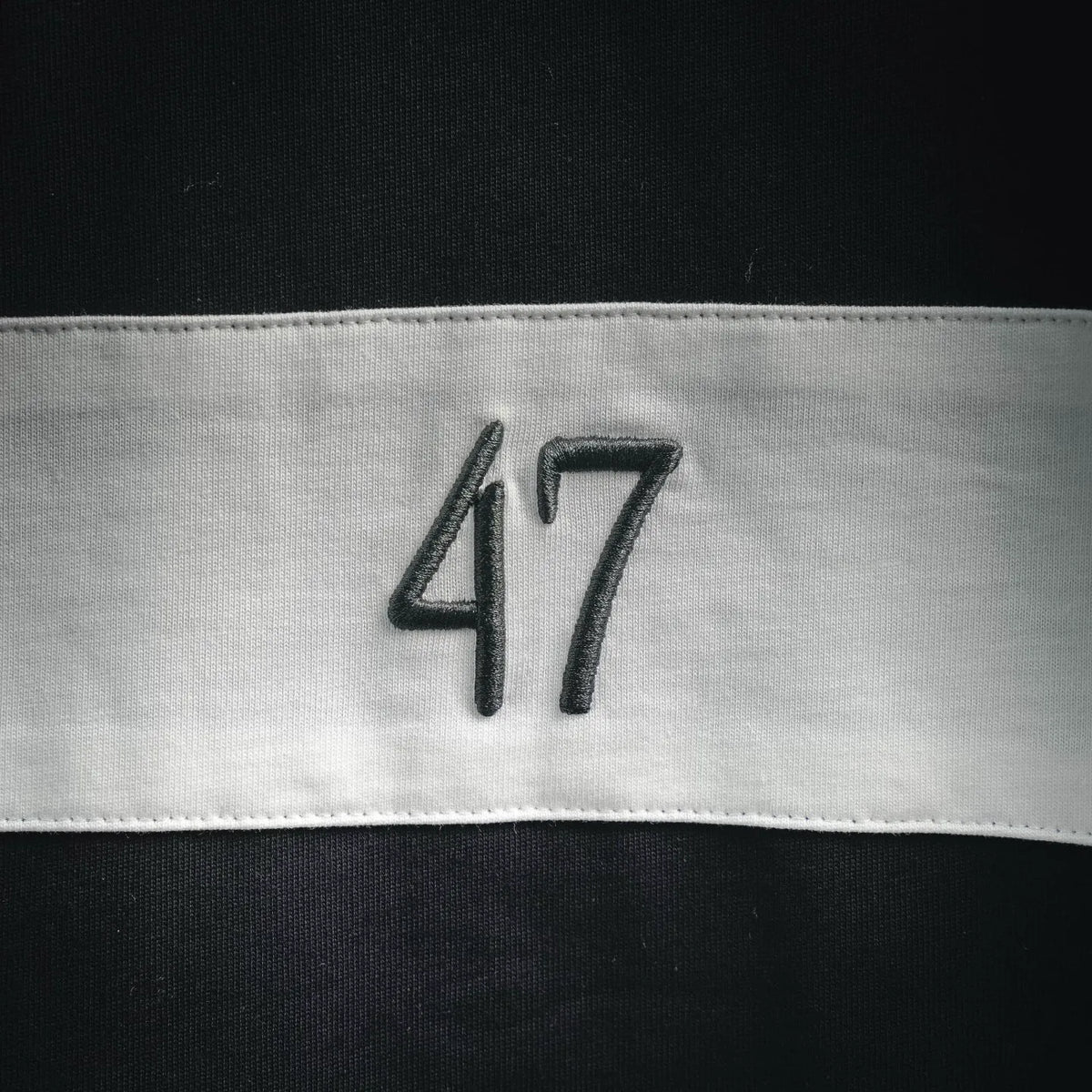 Close-up of '47' embroidery on a dark Dior T-shirt hem band.