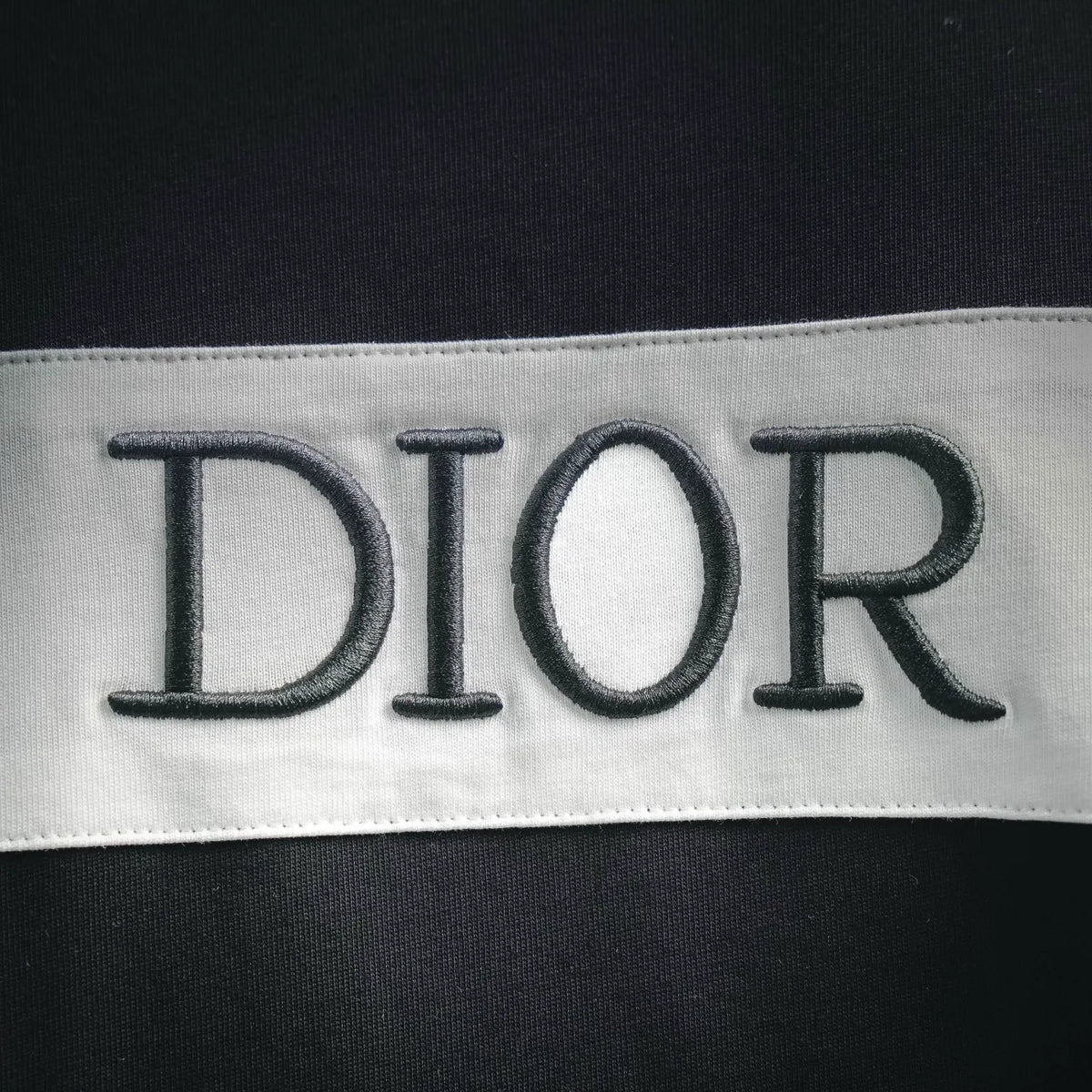 Close-up of 'DIOR' embroidery on the white band of a dark Dior T-shirt.