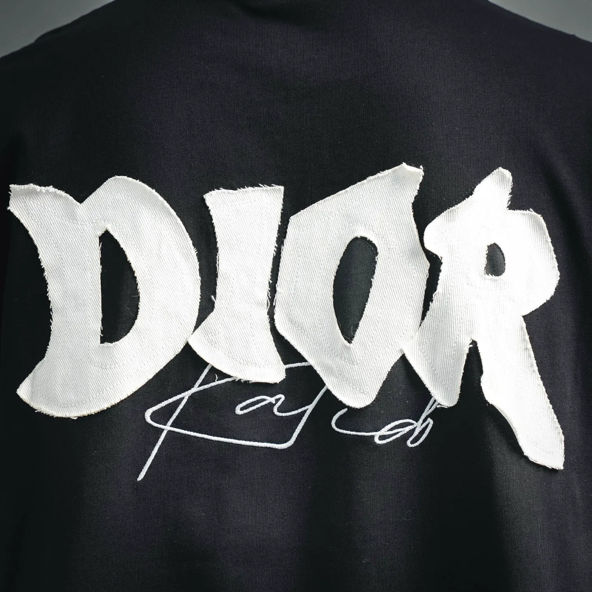 Close-up of white Dior logo embroidery on black short-sleeve T-shirt