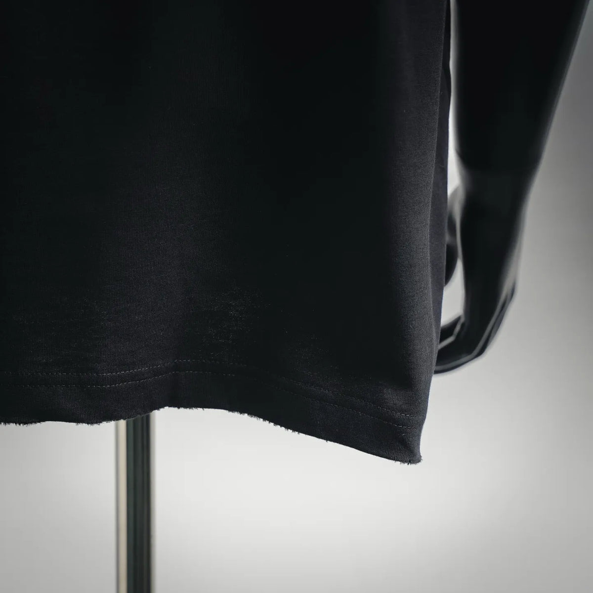 Black short-sleeve T-shirt hem with visible stitching and drape over a mannequin
