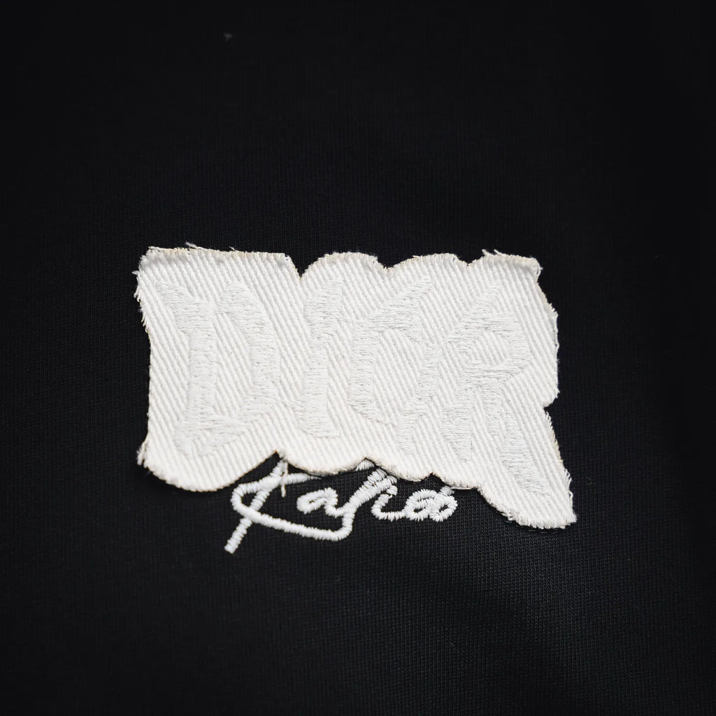 Close-up of white Dior logo patch with script stitching on black fabric