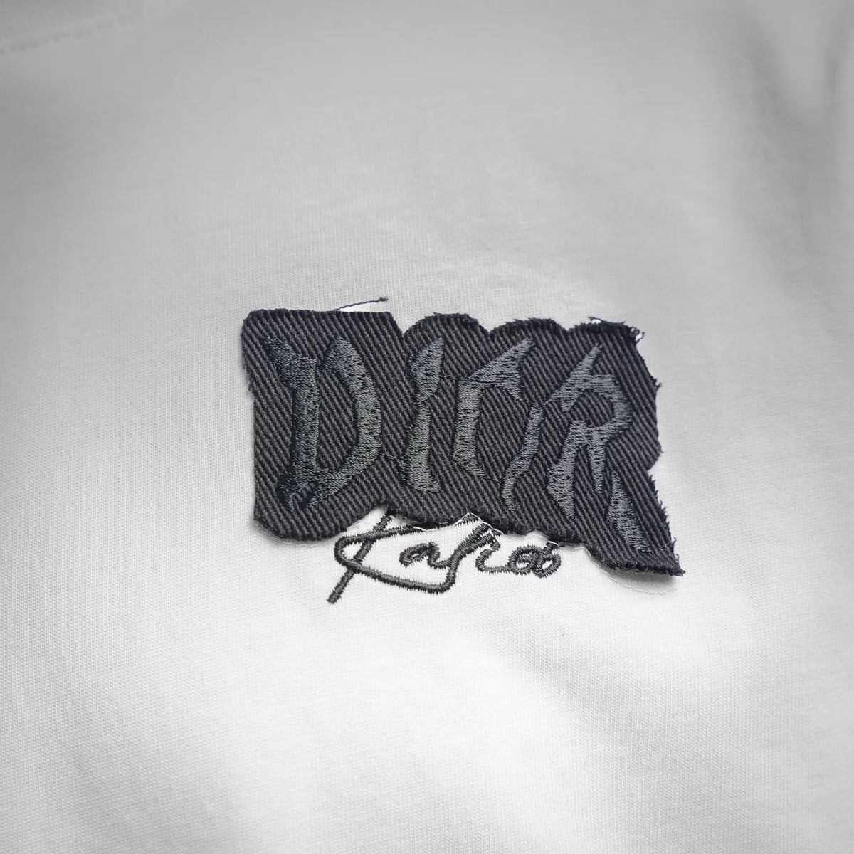 Black Dior embroidered logo patch on a white Dior T-shirt chest