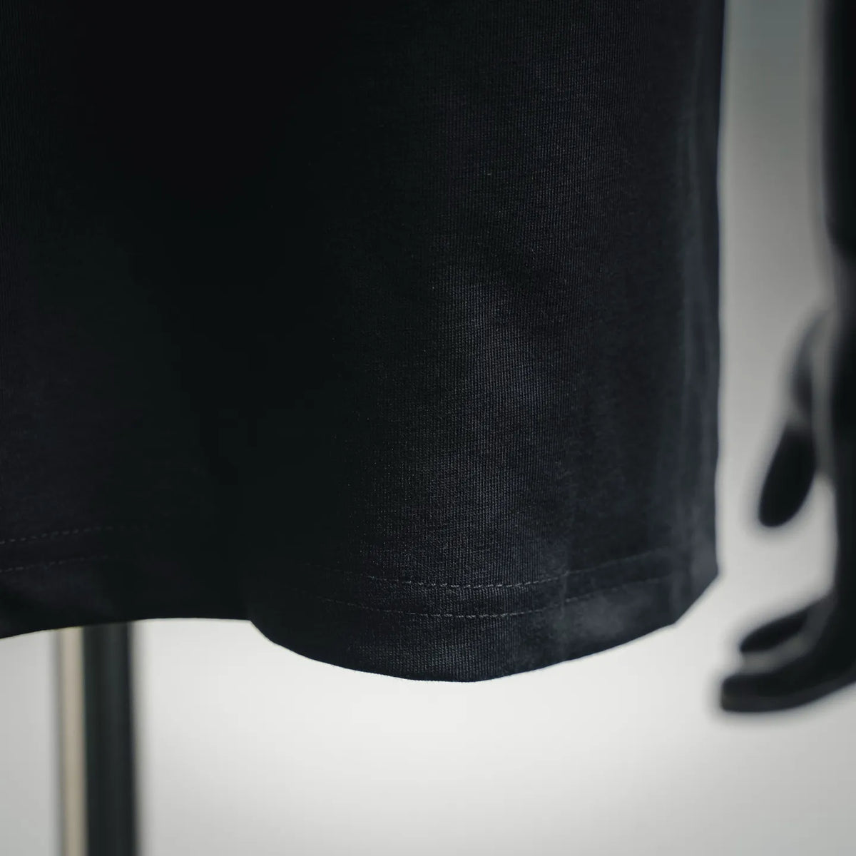 Dior crew-neck T-shirt hem close-up, dark fabric with stitched bottom edge