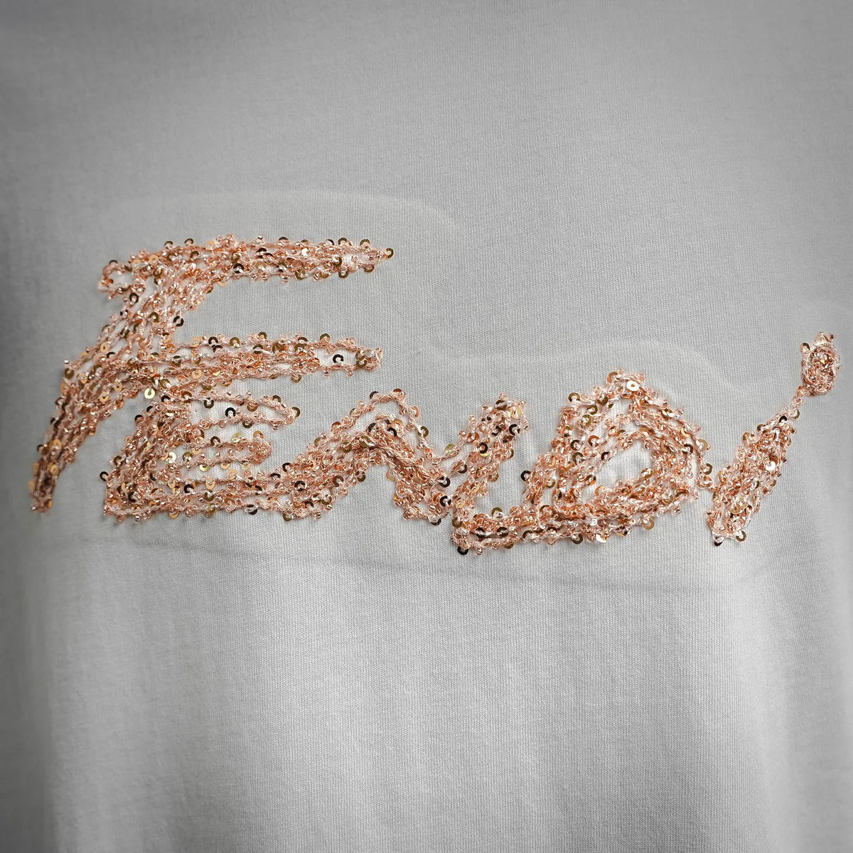 Close-up of gold sequin logo embroidery on white T-shirt